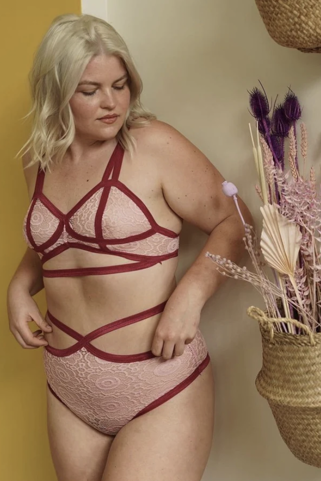 mid size model wearing a pink lace strappy bra and panty set with bold red piping 